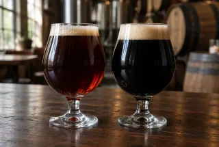 Deux verres de bière noire comparant un porter brun acajou et un stout presque noir, servis sur une table en bois dans une brasserie.